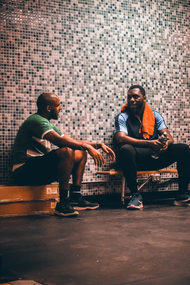 Two male athletes sitting in a locker room talking