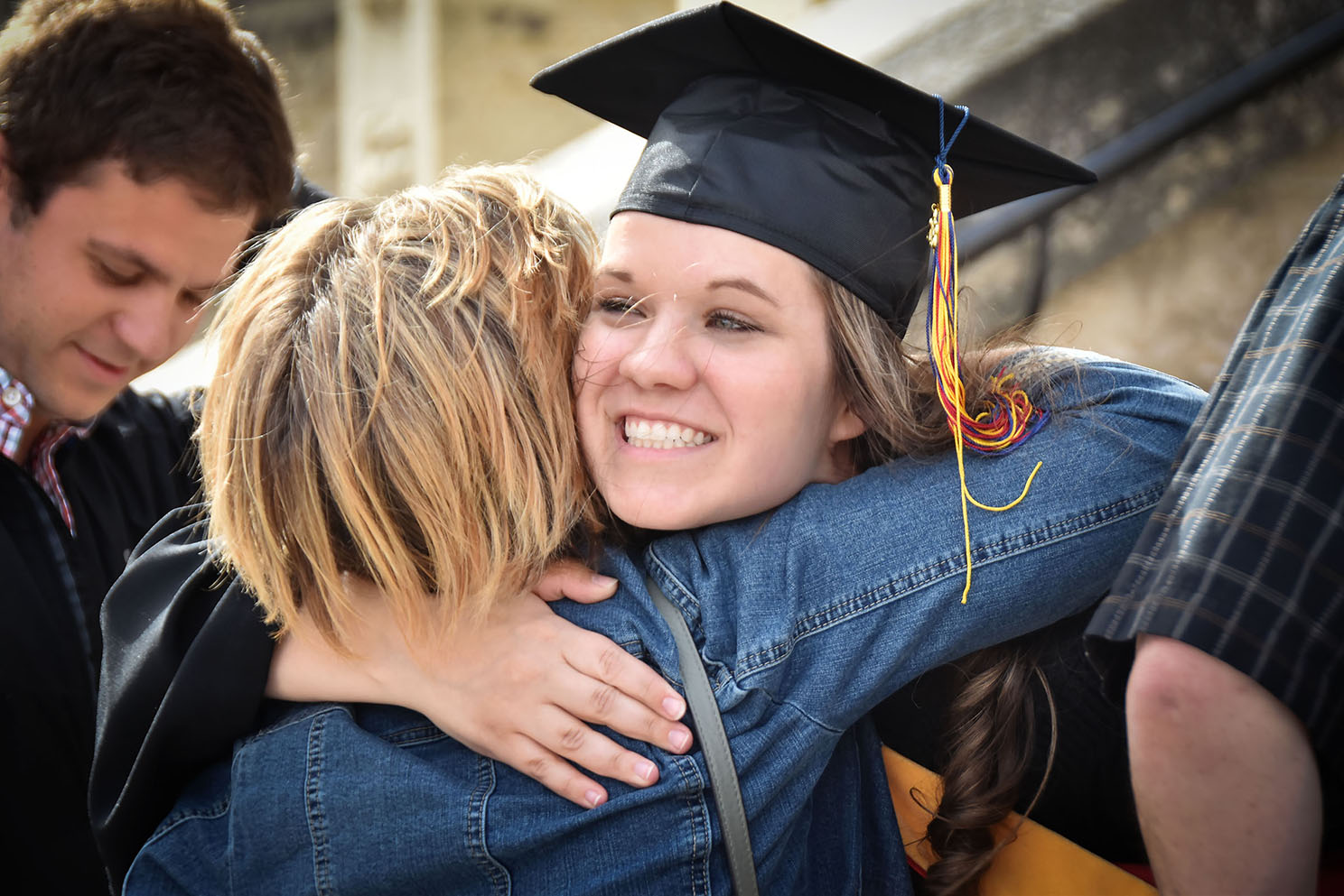 A student in her graduation cap, hugging a parent.