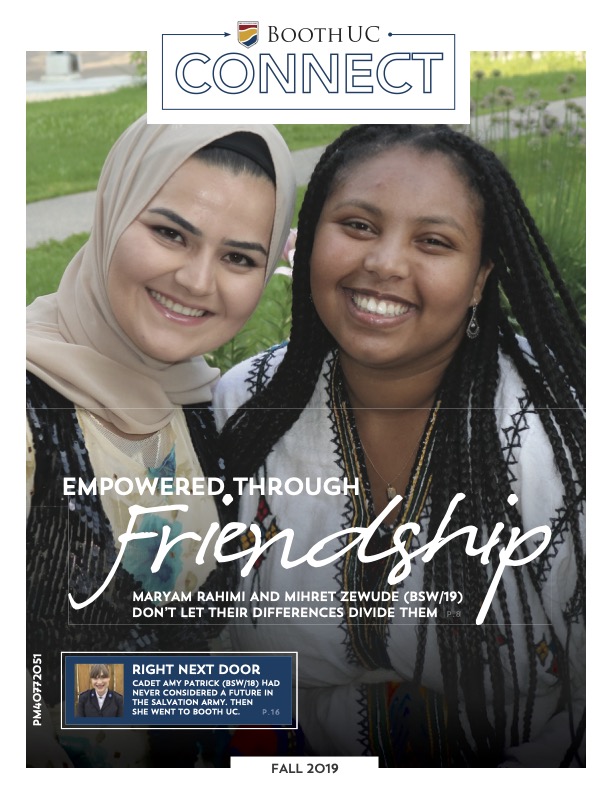 Two female students smiling and sitting in grass with text overlay that says "Empowered Through Friendship"