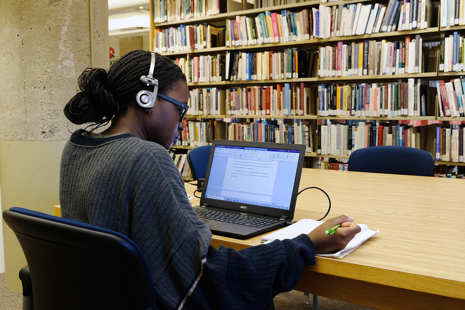 A female student wears headphones as she works in the library.
