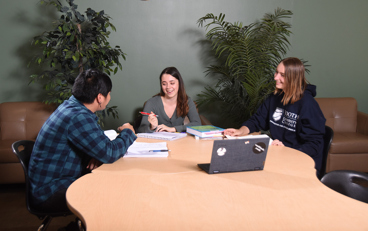 Three students working together at a table with papers and textbooks.
