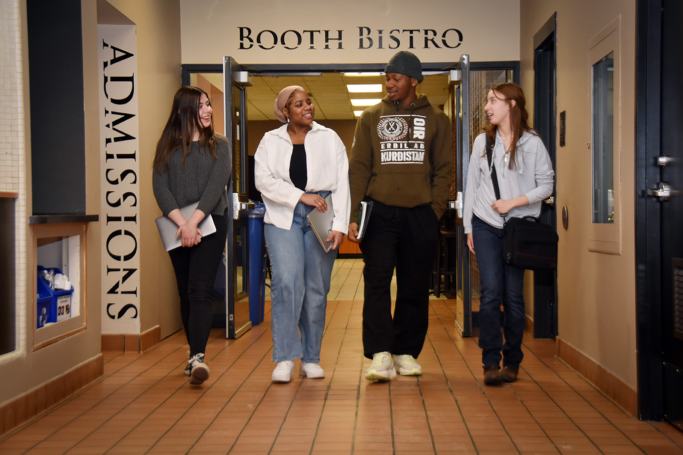 Four students holding textbooks walk together in a hallway.