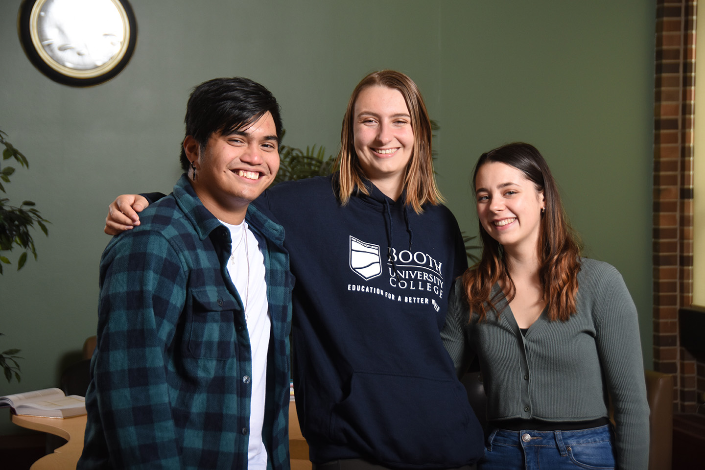 Three university students with arms around each other, smiling, looking at the camera.