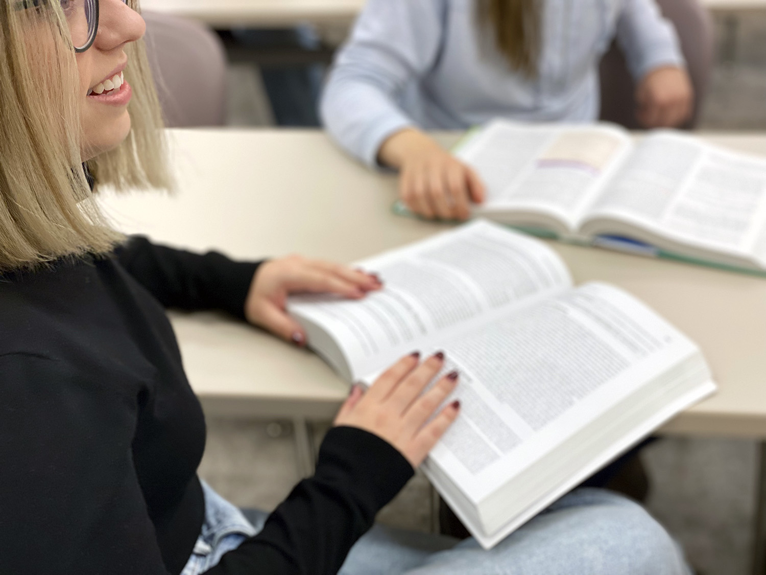 A female student sits at a desk with her hands on an open textbook.