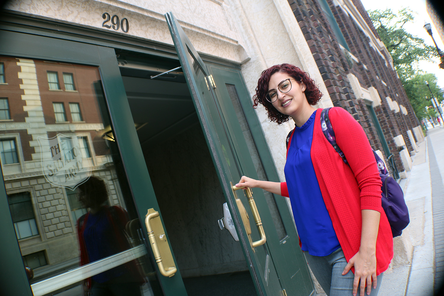 A female student smiles at the camera as she pulls the front door open.