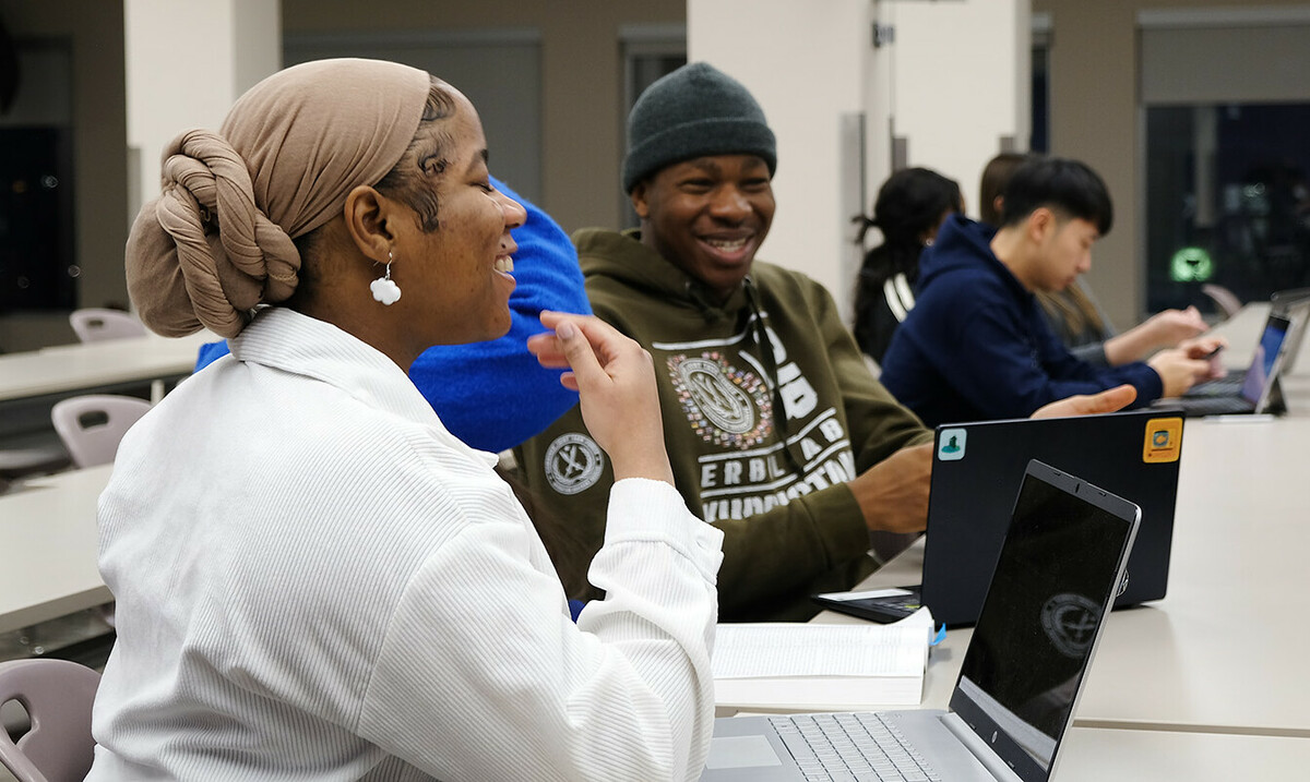 Students sitting at a desk with their laptop computers, laughing together.