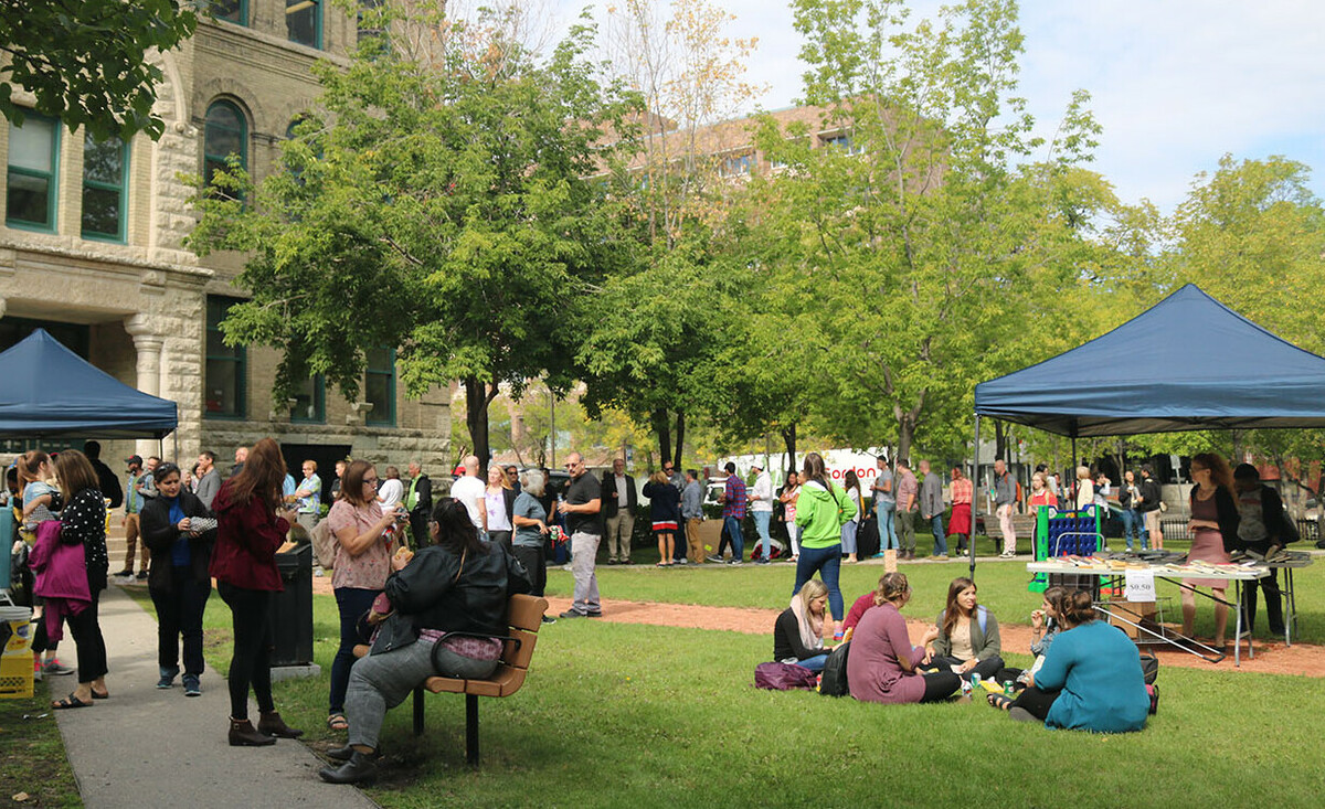 People gathered in green space outside the campus. Some people are sitting in small groups on the grass and others are standing and talking.