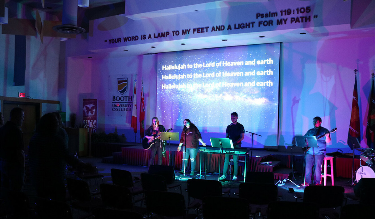 Four students sing at microphones with lights dimmed and a projector shining lyrics behind them.