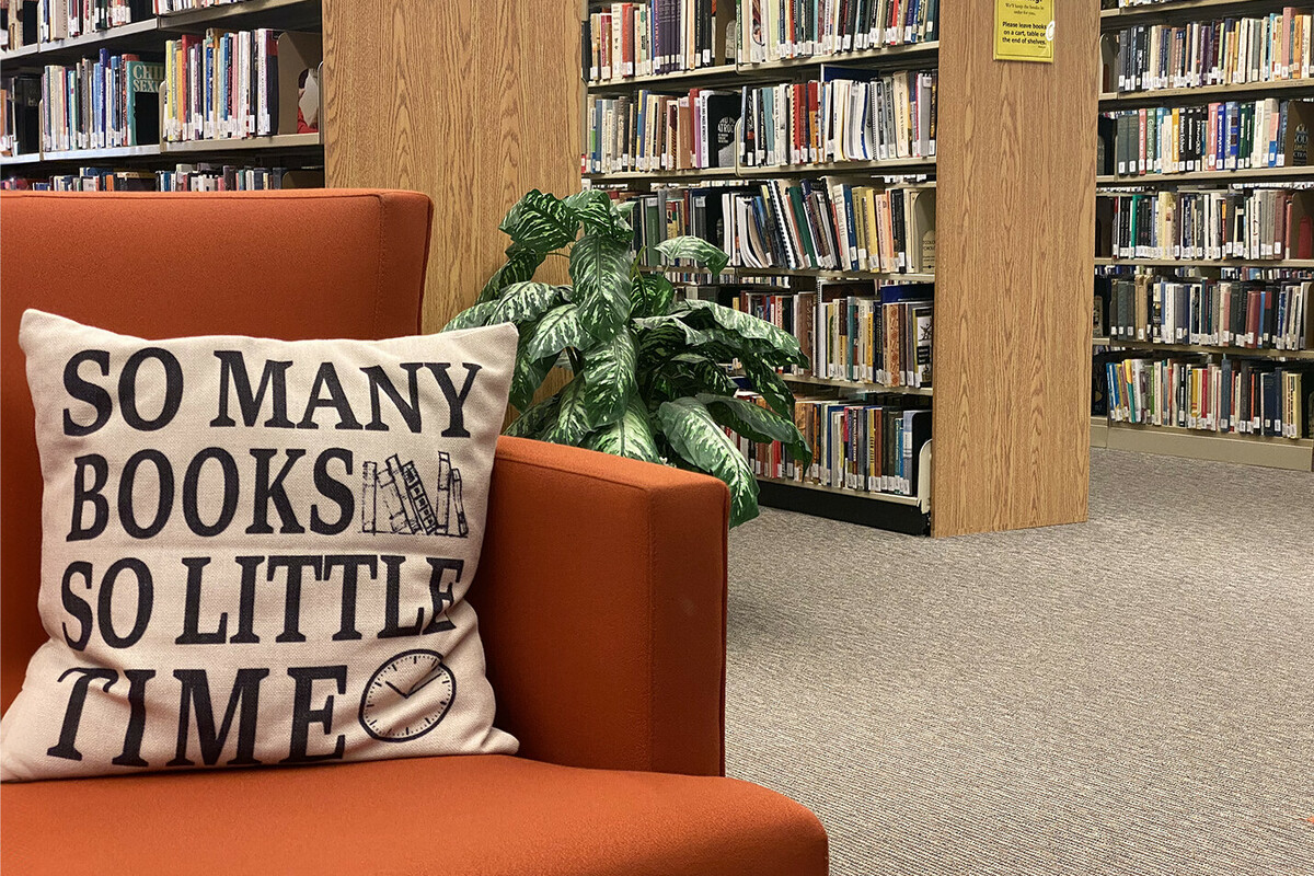 A cushion on a chair reads So many books, so little time.