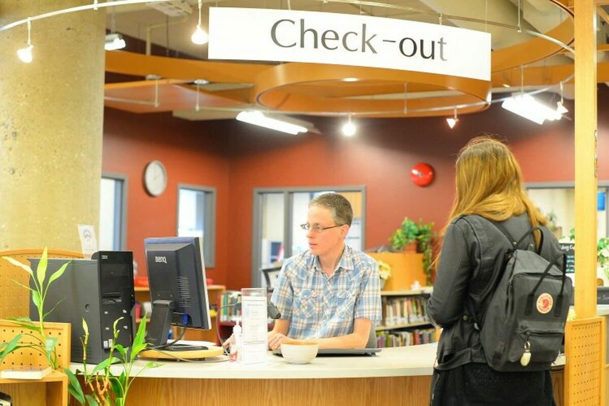 A student at the library check-out desk talking to a librarian
